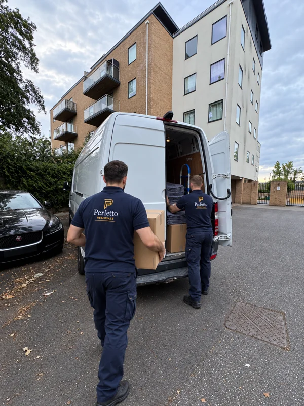 Illustrative scene of two workers in Perfetto uniforms seen from behind handling boxes and moving blankets at a van